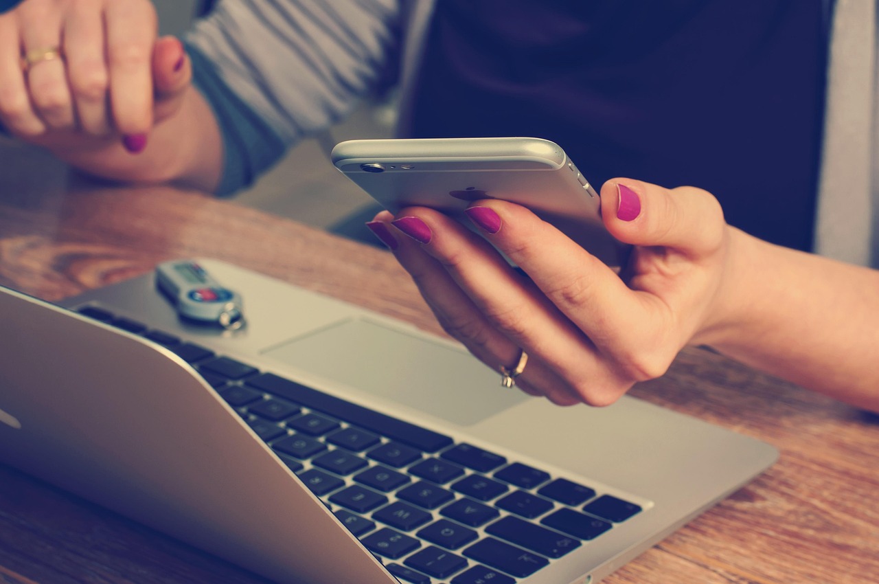 Person holding phone with laptop showing multiple device consistency check