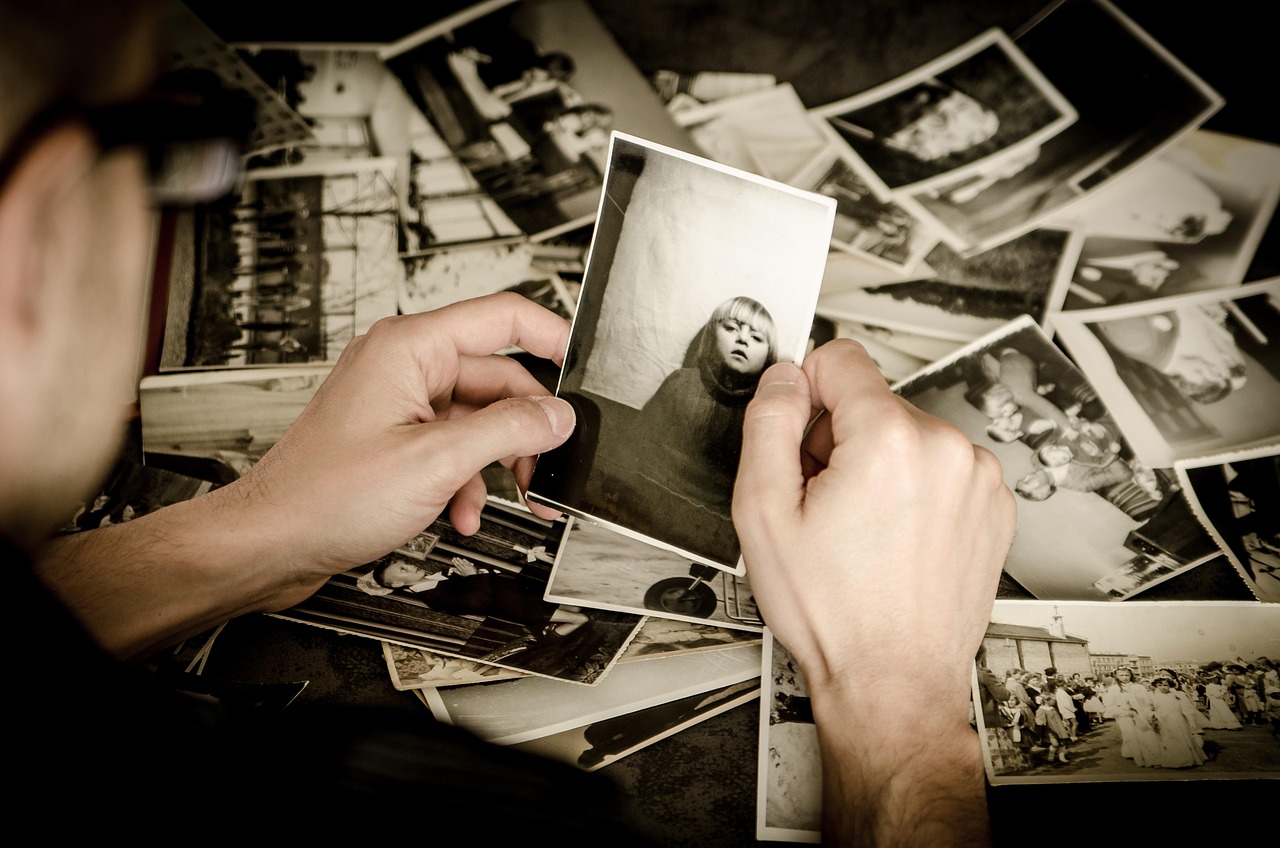 Hands holding vintage family photograph among collection of old photos, representing inherited expressions and linguistic legacy from parents and grandparents