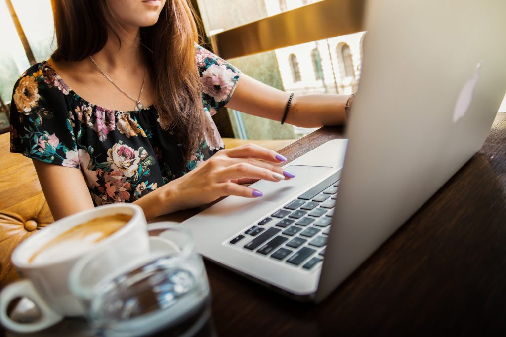 A woman typing on a laptop in a café with a coffee nearby — writing with focus and intention, one reader in mind.